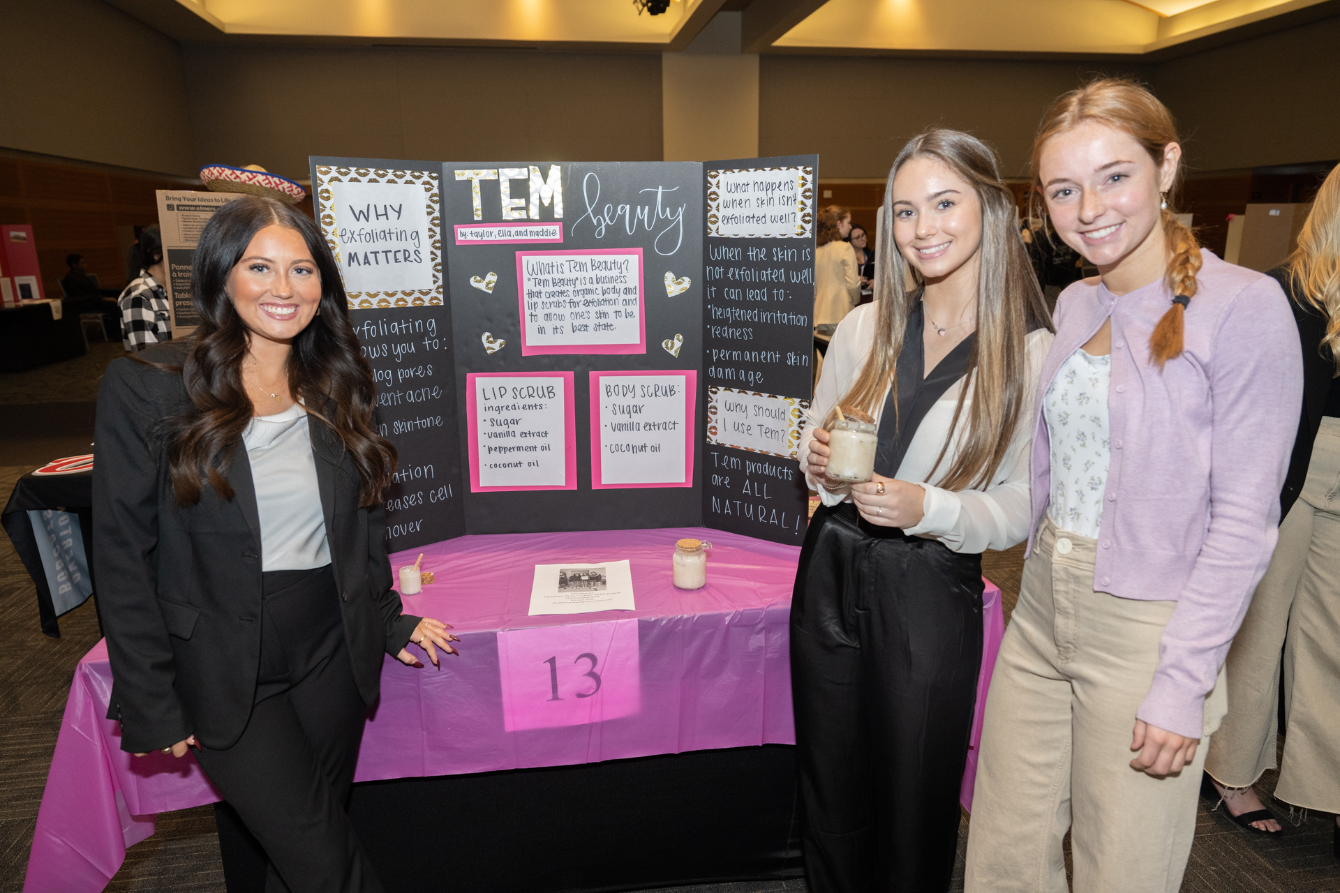 3 female highschool students stand in front of their business plan poster. The poster reads, "TEM beauty. Why exfoliating matters."