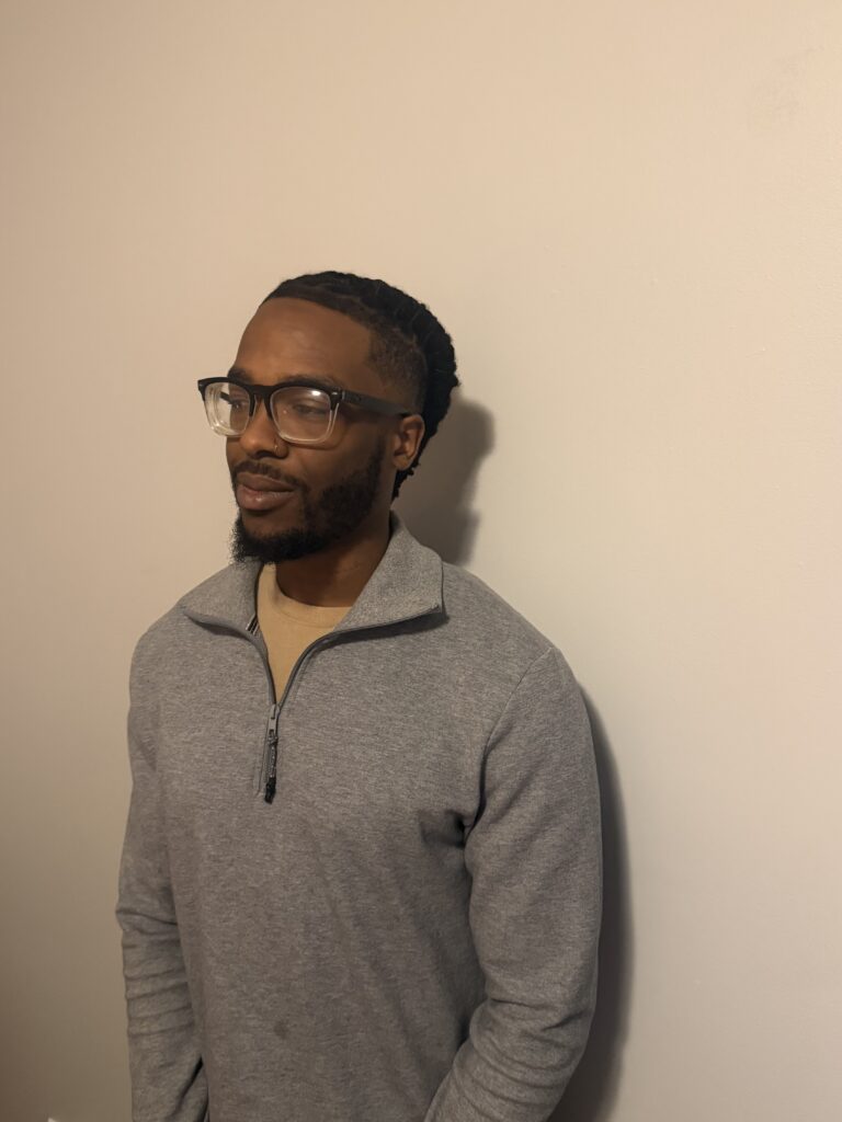 Juavante in front of a wall in a grey quarter zip, with a slight shadow behind him