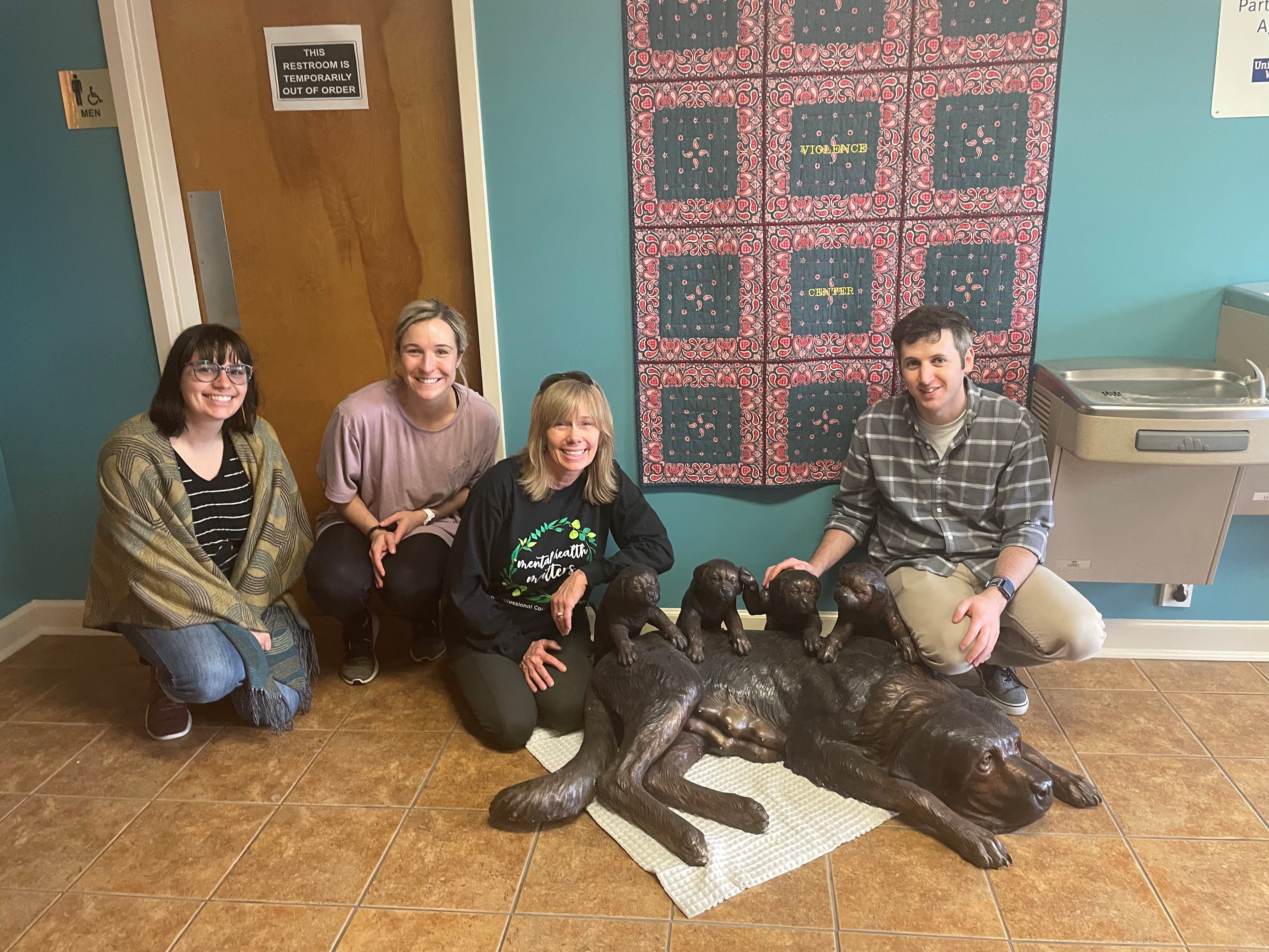 Group of member of Chi Sigma Iota posing next to bronze statue of dog with puppies