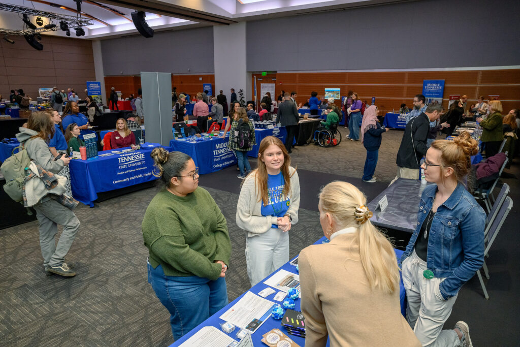Photo of a two girls at the grad fair speaking to two women at a table
