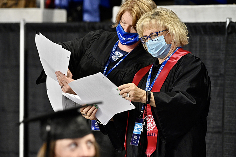 MTSU commencement heralds Allison McGoffin, left, and Pat Thomas, wearing their masks and "Team Grad" ID badges, check their seating charts Friday, May 7, inside Murphy Center to ensure that the spring 2021 graduates are in the correct order when their names are called to cross the stage. McGoffin, assistant to University Provost Mark Byrnes, and Thomas, assistant to the university's Board of Trustees and to retired Lt. Gen. Keith M. Huber, senior adviser for veterans and leadership Initiatives, are members of a well-practiced crew helping students returning to Murphy Center May 7-9 for the first time since 2019 for a three-day, 10-event, socially distanced commencement weekend. (MTSU photo by J. Intintoli)