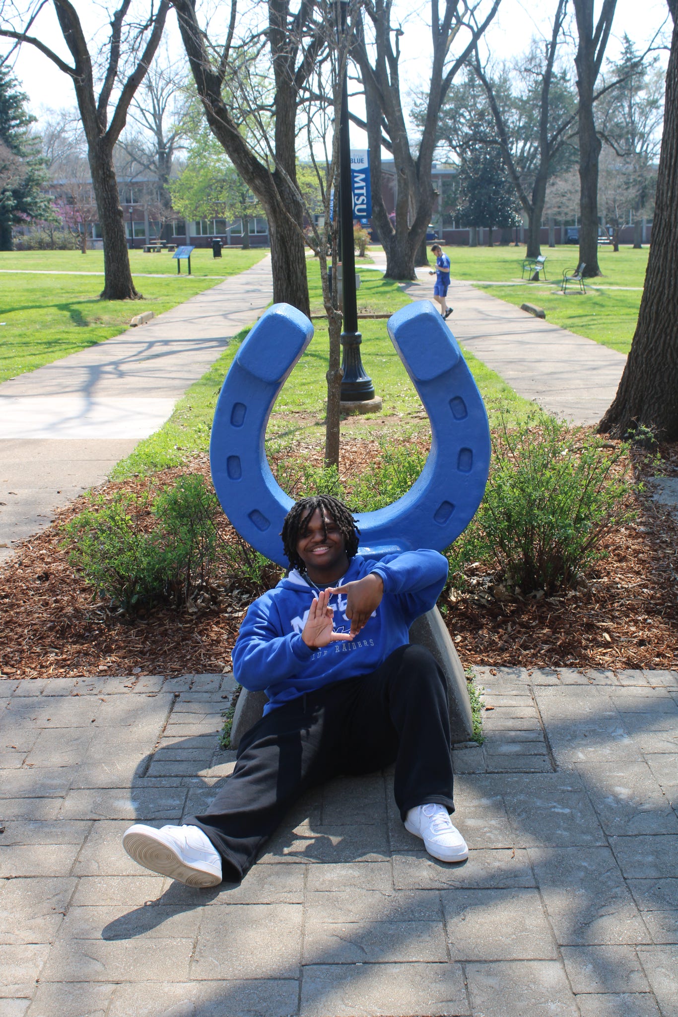 Photo of Aden Walton sitting in front of the blue horseshoe in Walnut Grove at MTSU.