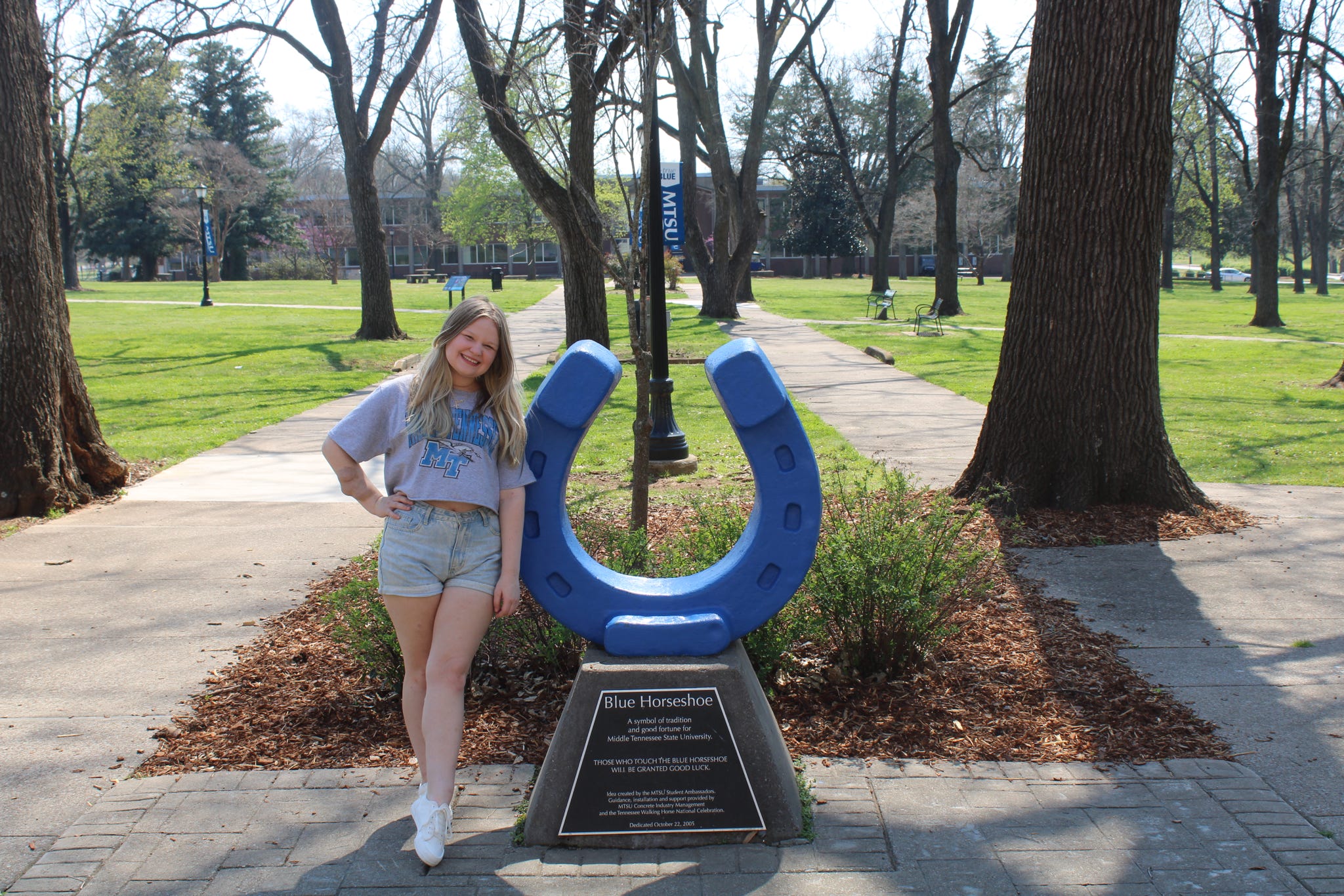 Photo of Brooklyn Latimer standing beside the blue horseshoe in Walnut Grove at MTSU.