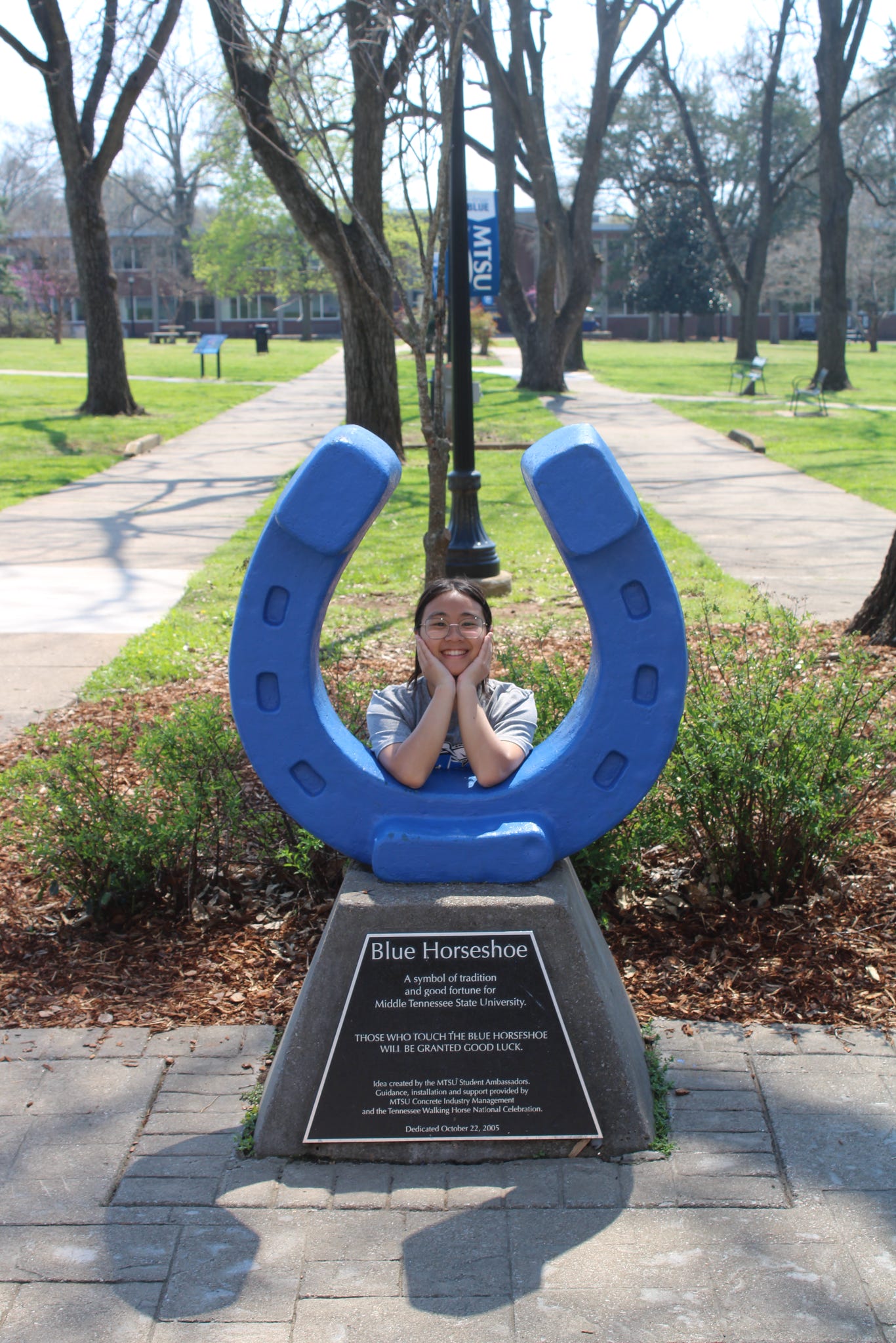 Photo of Fena Phengmany standing behind the blue horseshoe in Walnut Grove at MTSU.
