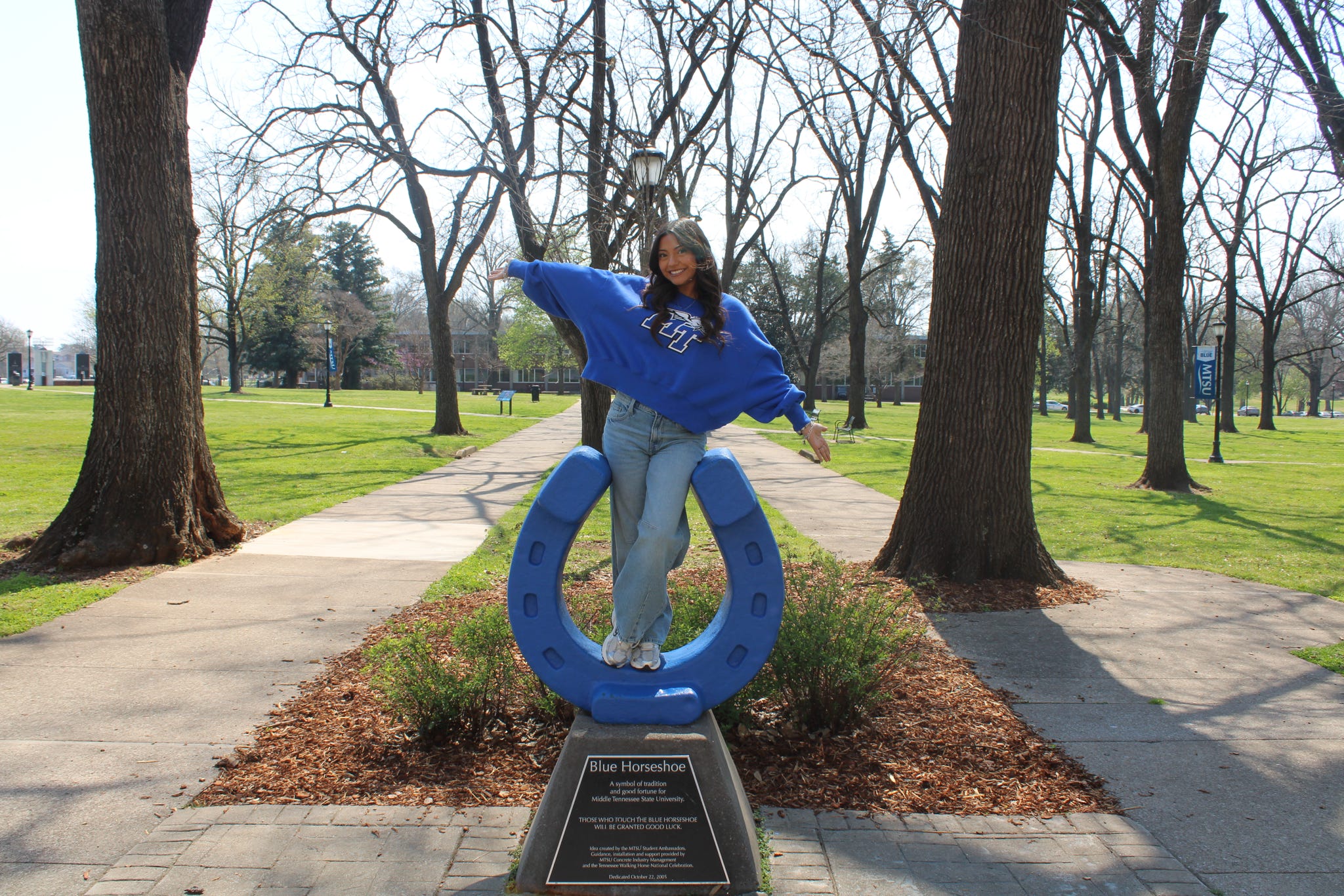 Photo of Jeslyn Vasquez standing on top of the blue horseshoe in Walnut Grove at MTSU.