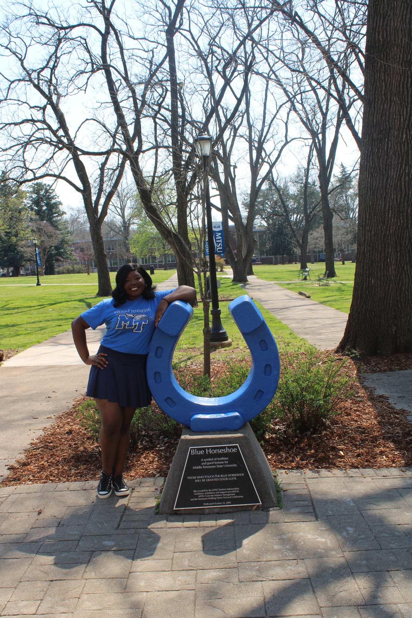 Photo of Kat Woodland standing beside the blue horseshoe in Walnut Grove at MTSU.