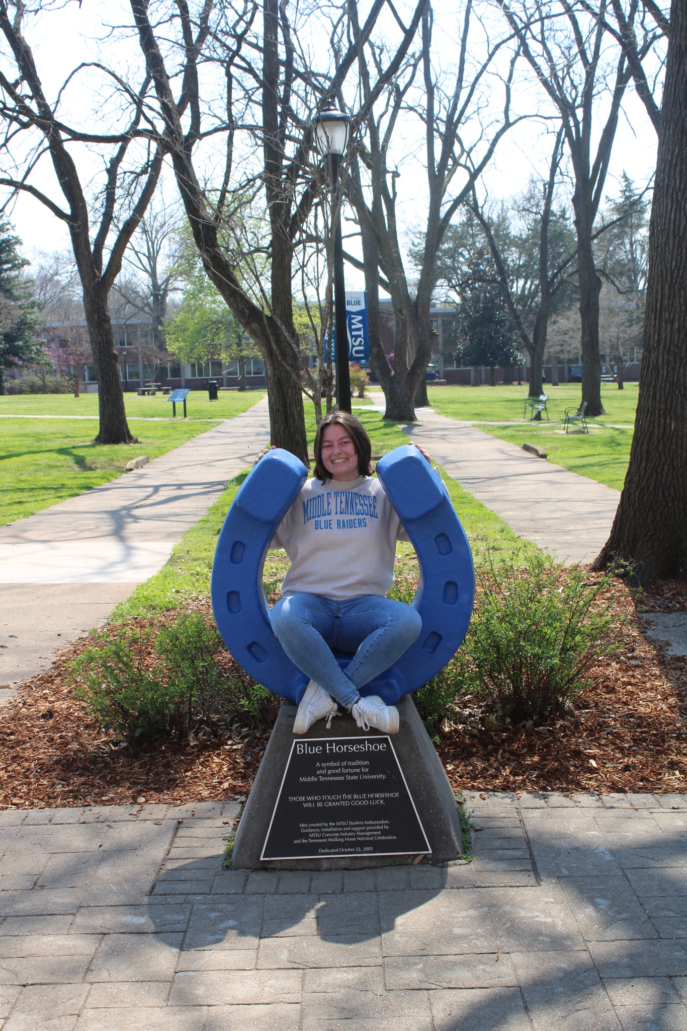 Photo of Kenzie Herrick sitting on the blue horseshoe in Walnut Grove at MTSU.