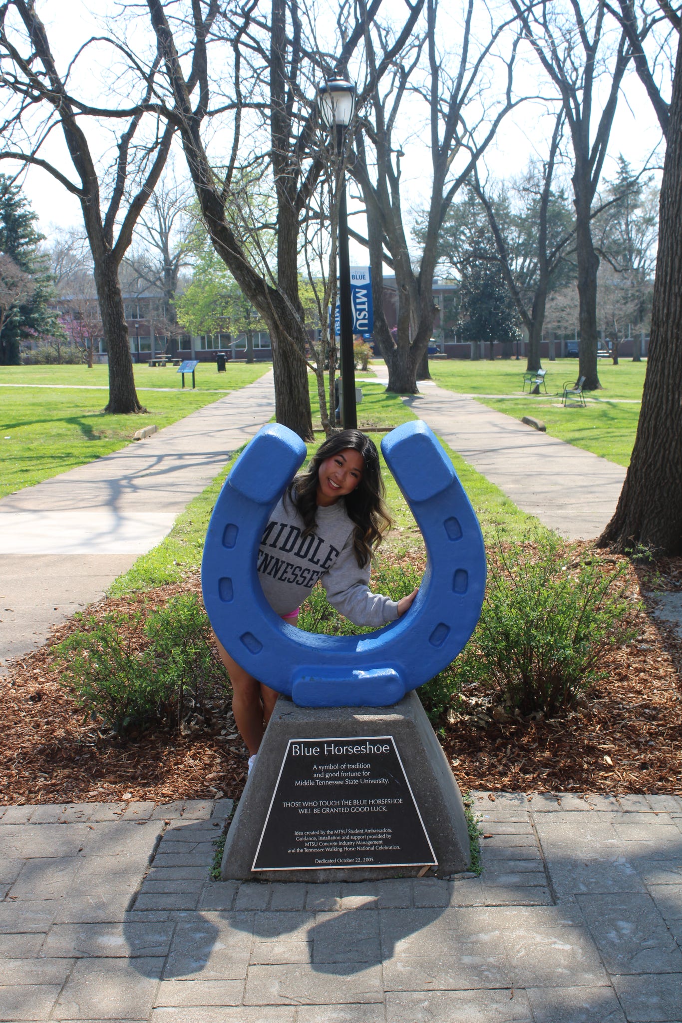 Photo of Lily Maiuri standing behind the blue horseshoe in Walnut Grove at MTSU.