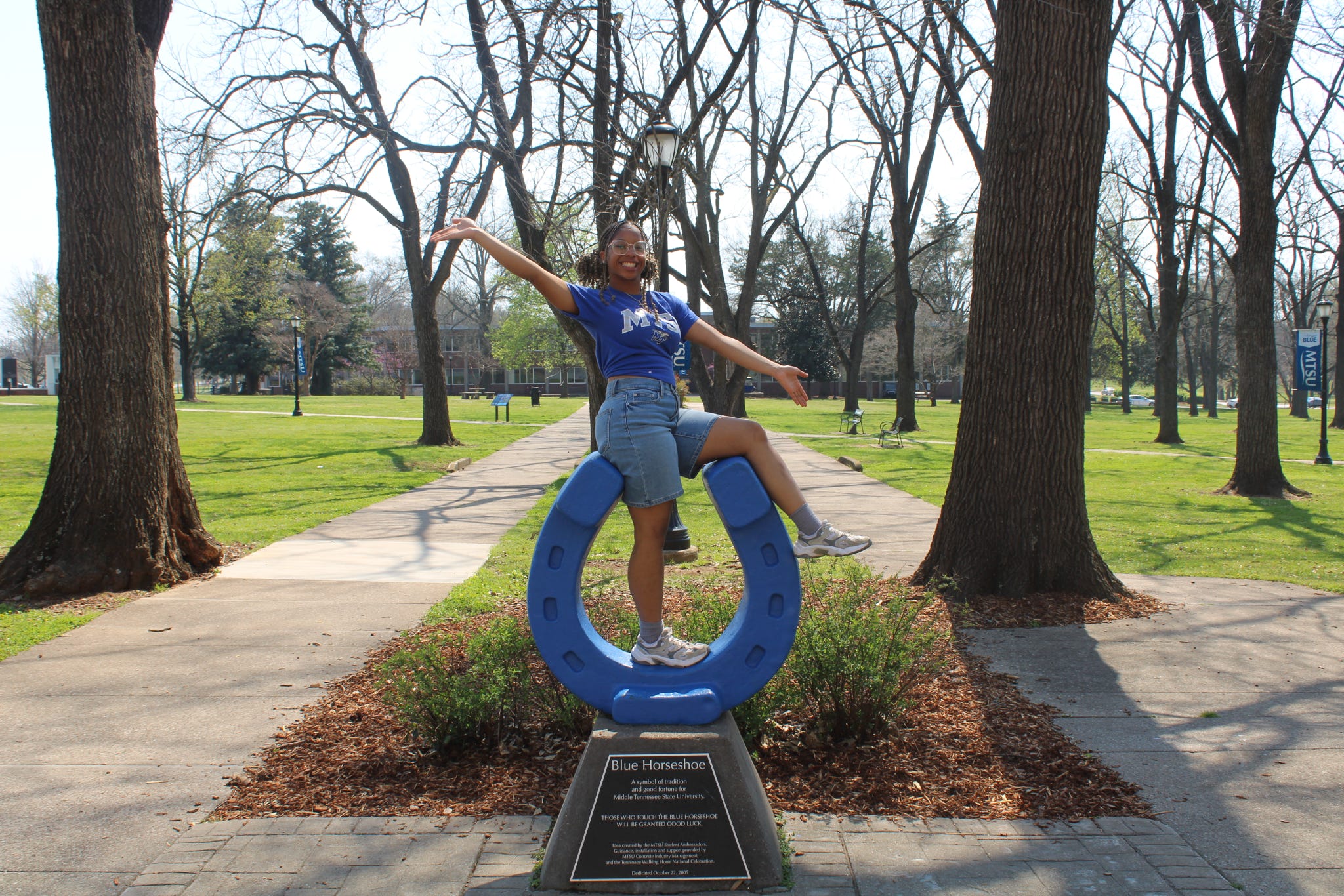 Photo of MJ Wilson sitting on top of the blue horseshoe in Walnut Grove at MTSU.