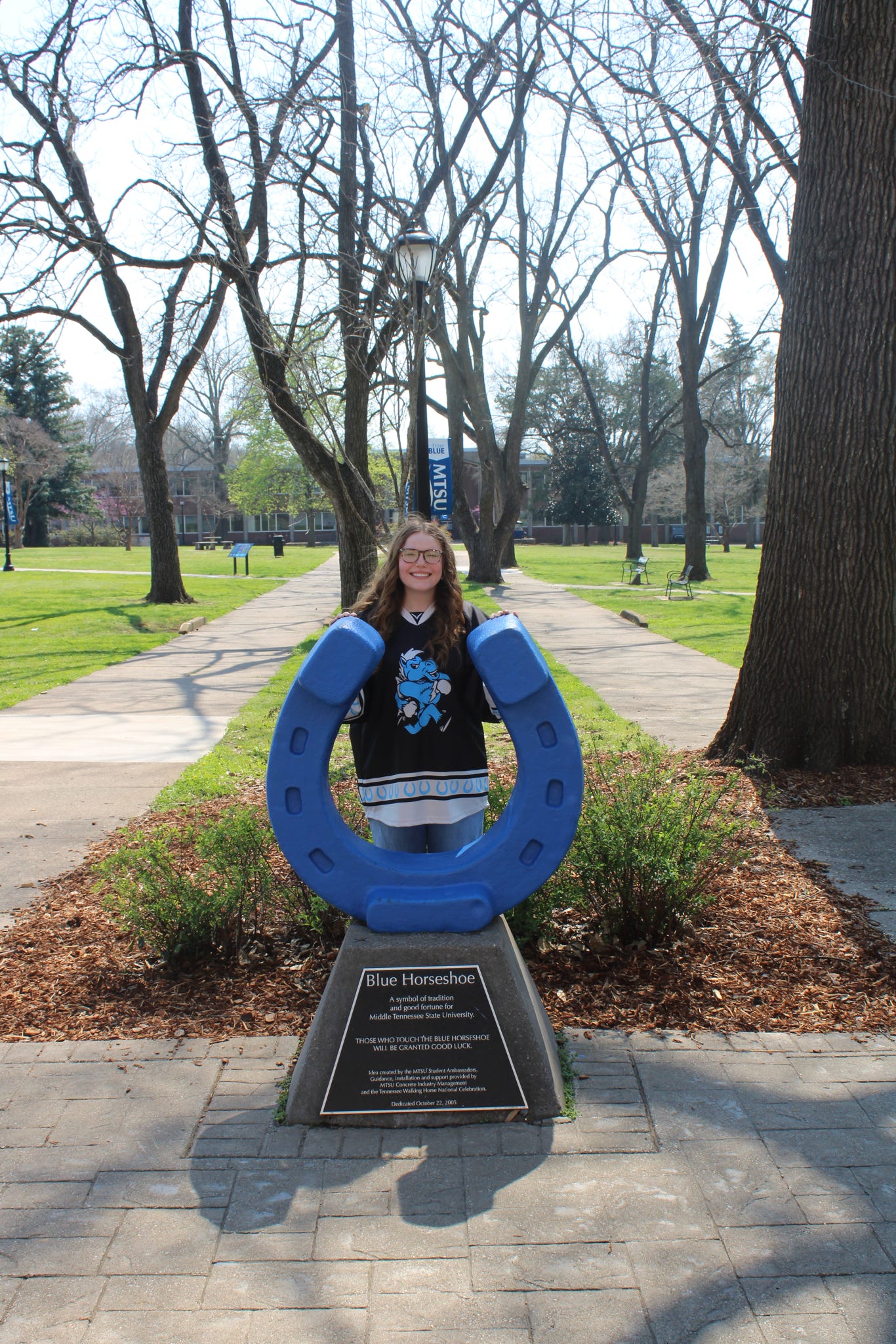 Photo of MacKenzie Chambers standing behind the blue horseshoe in Walnut Grove at MTSU.