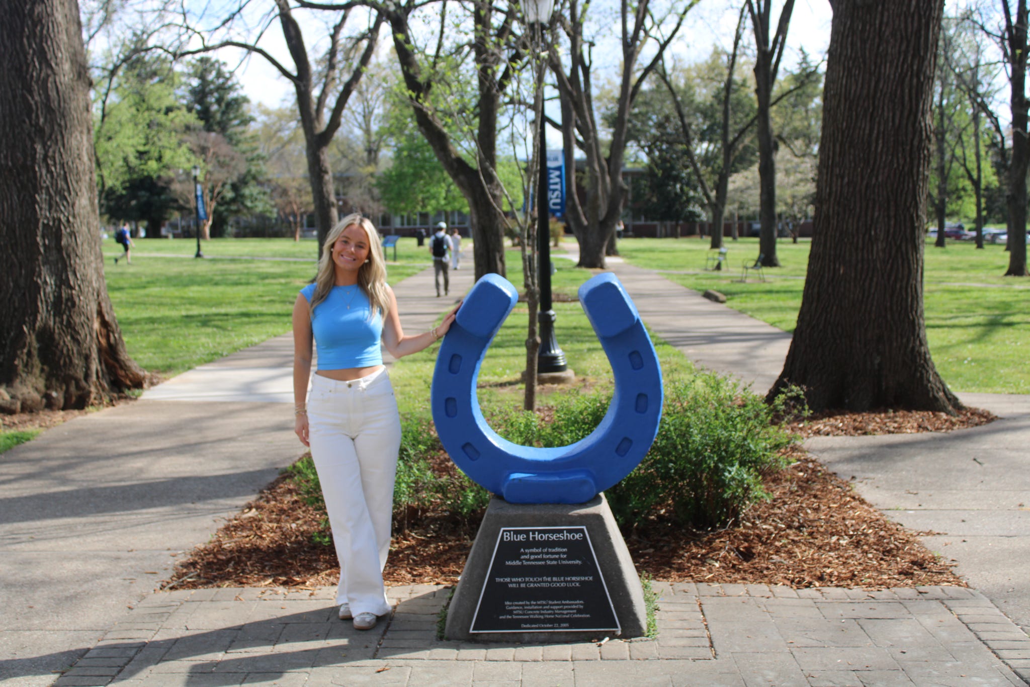 Photo of Maddy Couey standing beside the blue horseshoe in Walnut Grove at MTSU.