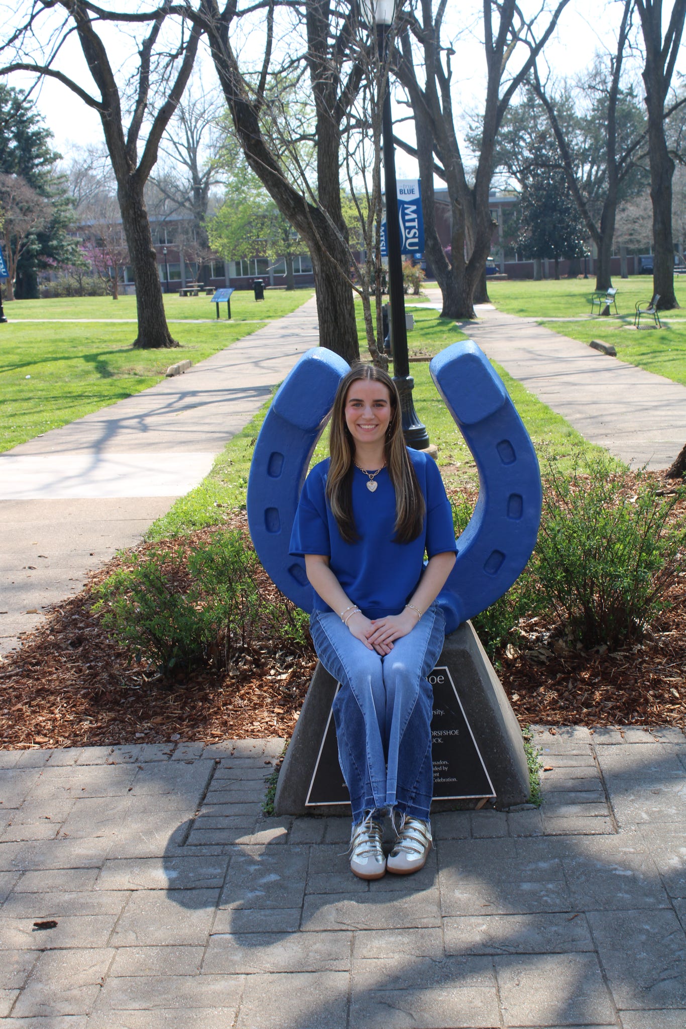 Photo of Madison Rainier sitting on the blue horseshoe in Walnut Grove at MTSU.