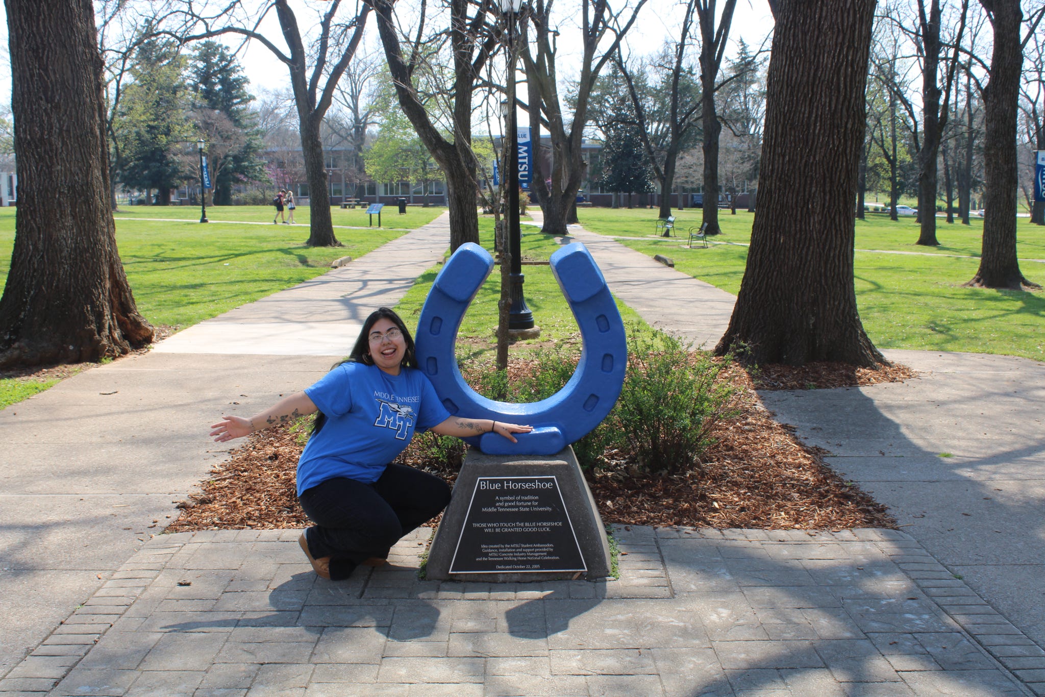 Photo of Olivia Travers squatting beside the blue horseshoe in Walnut Grove at MTSU.