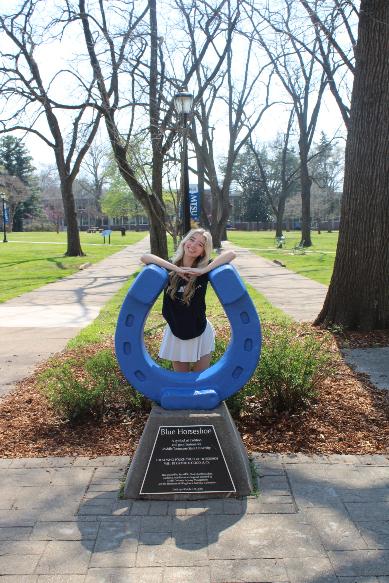 Photo of Rylee Grady standing behind the blue horseshoe in Walnut Grove at MTSU.