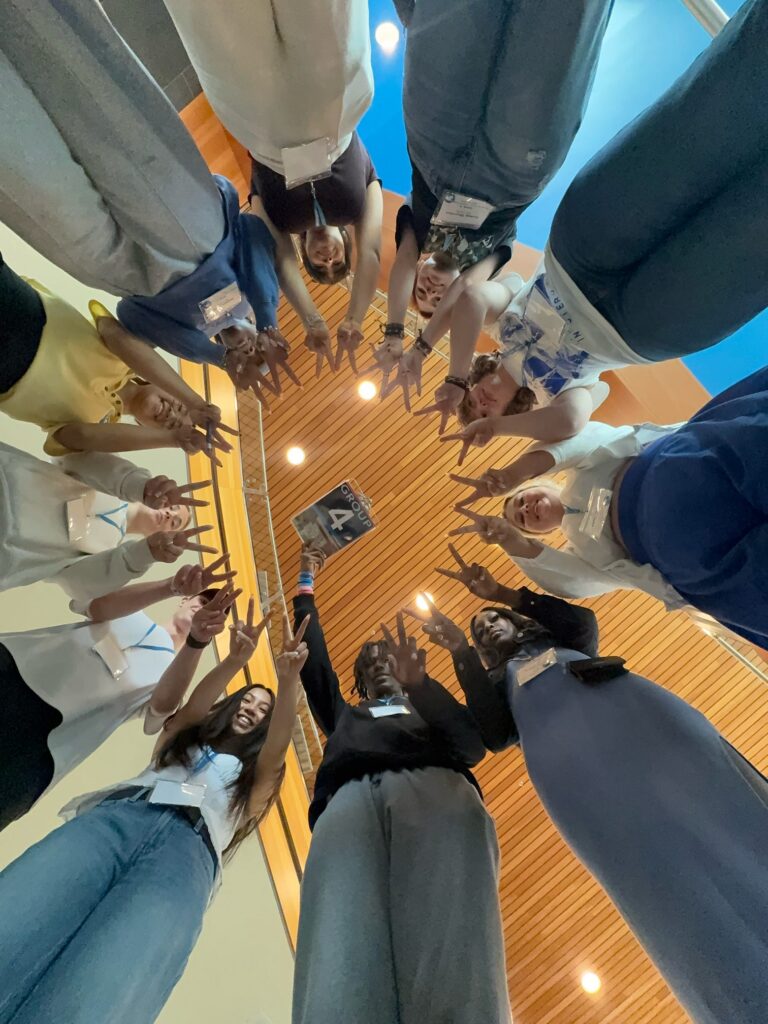 Students in Group 4 of orientation standing in a circle holding up two fingers on each hand with their Student Orientation Assistant.