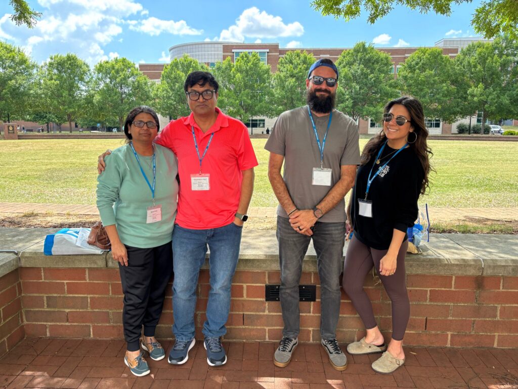 Four people posing for a photo at orientation outside the Student Union and College of Education building.