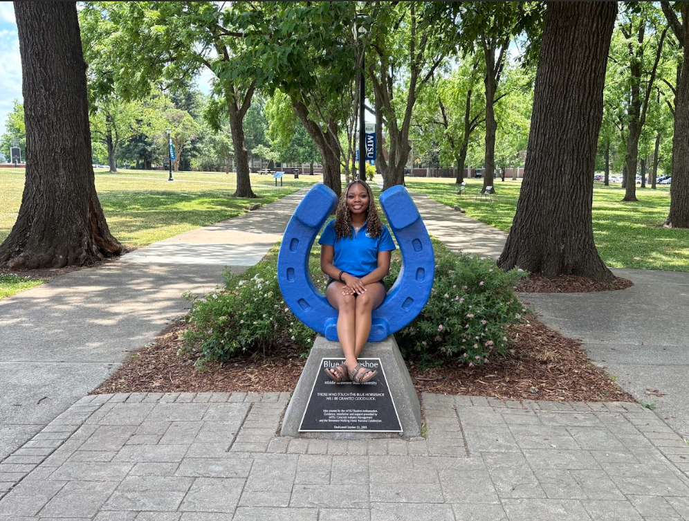 Photo of Aleila Coplin sitting on the blue horseshoe in Walnut Grove at MTSU.