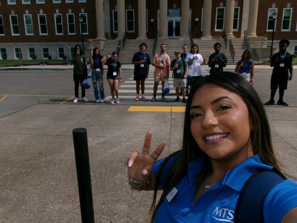 Students attending orientation posing outside the renovated Kirksey Old Main with their Student Orientation Assistant.