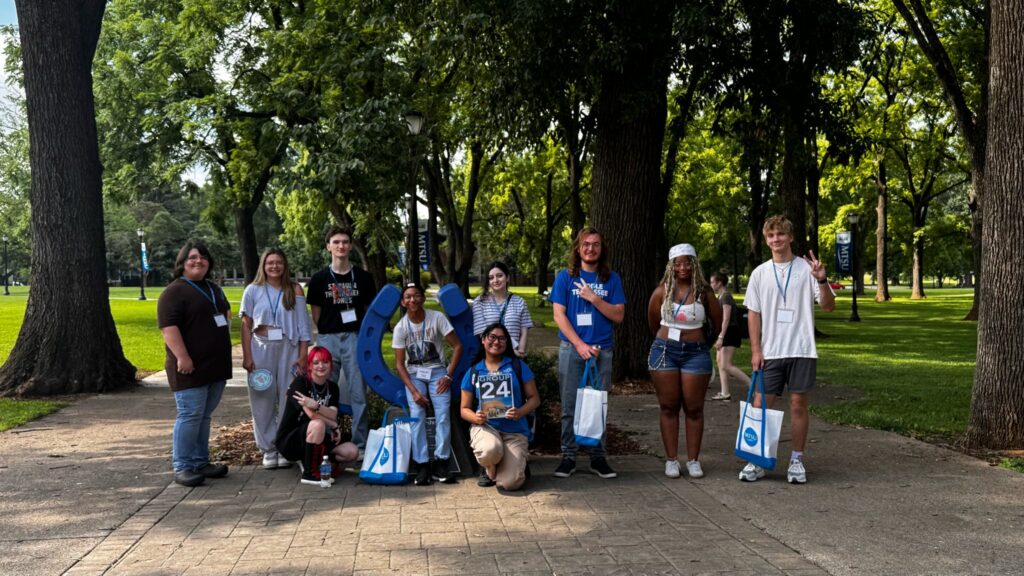 Students in Group 24 of orientation posing for a photo at the blue horseshoe at MTSU with their Student Orientation Assistant.