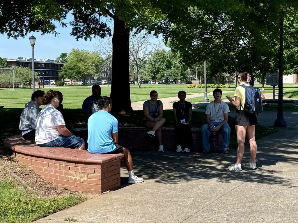 Students attending orientation sitting in a shaded semi-circle while their Student Orientation Assistant leads a conversation.