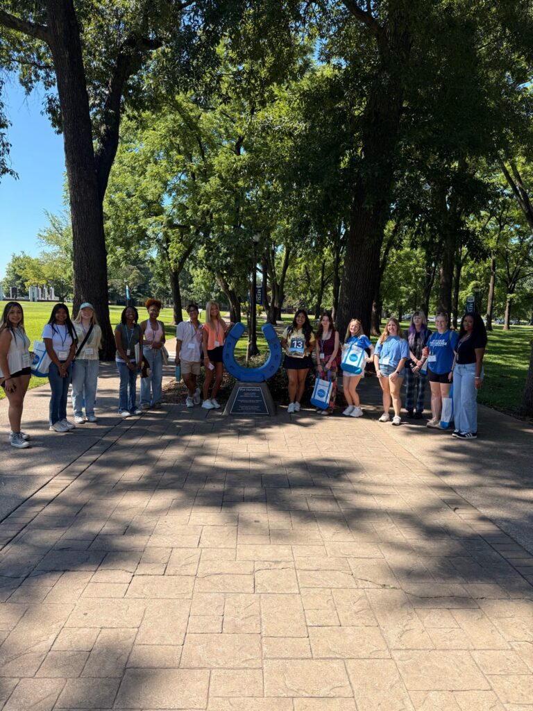 Students in Group 13 of orientation posing for a photo at the blue horseshoe at MTSU with their Student Orientation Assistant.