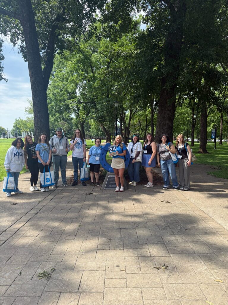 Students in Group 24 of orientation posing for a photo at the blue horseshoe at MTSU with their Student Orientation Assistant.