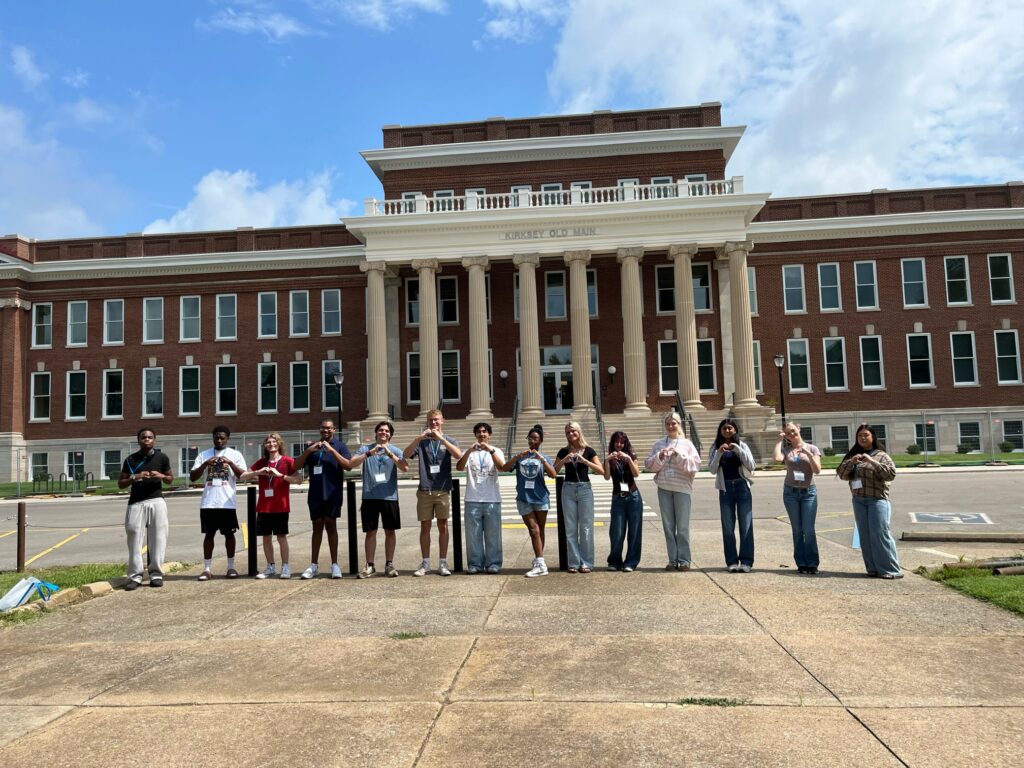 Students attending orientation standing outside the renovated Kirskey Old Main forming hearts with their hands.