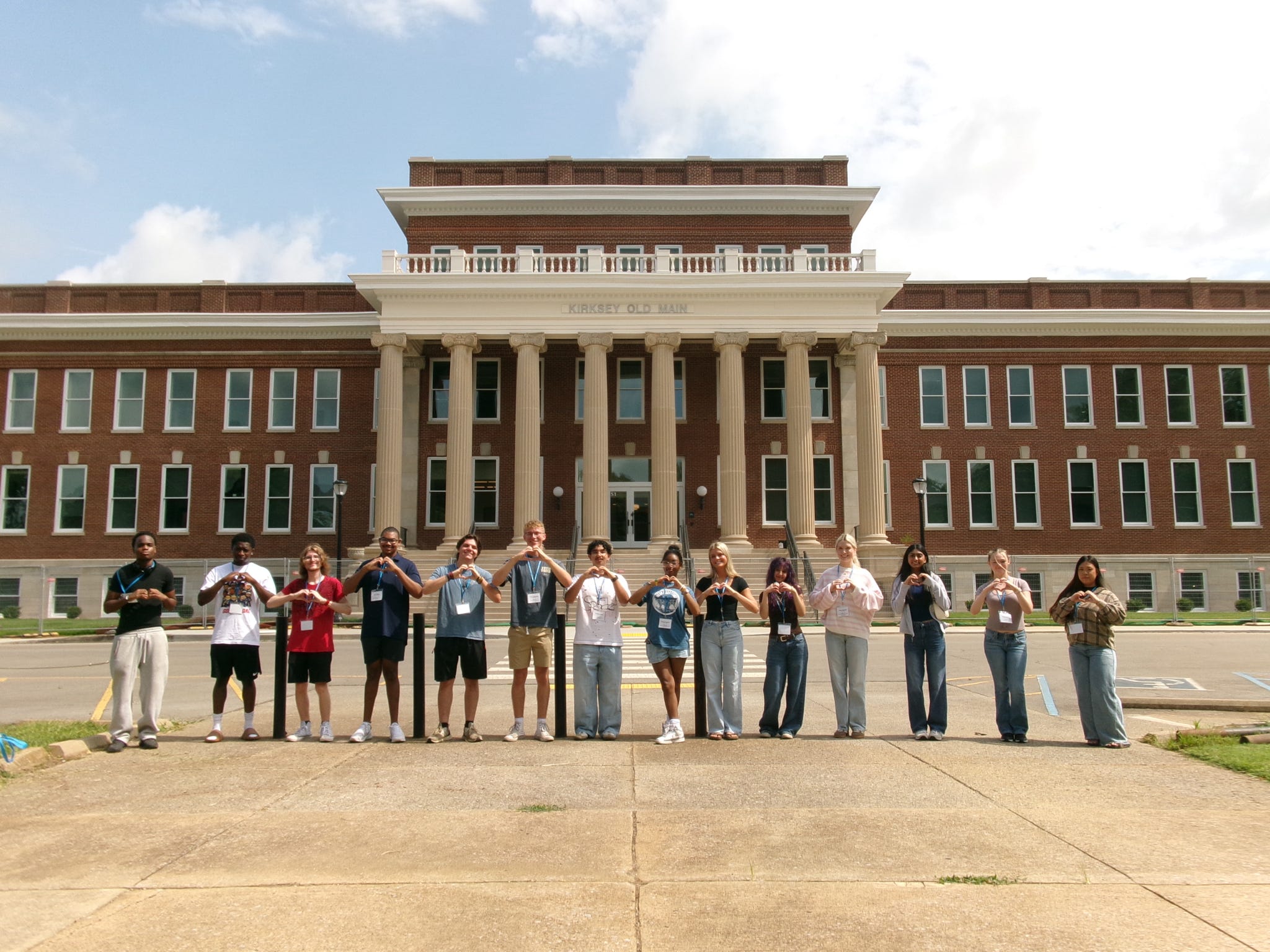 Students attending orientation standing outside the renovated Kirskey Old Main forming hearts with their hands.