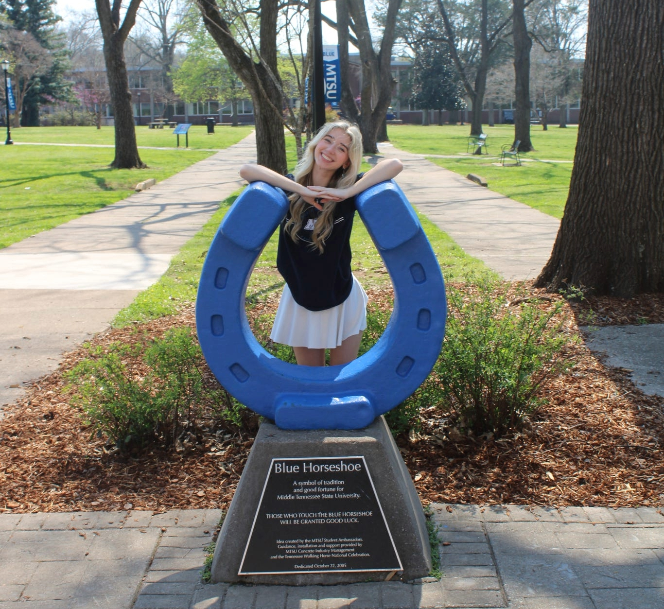 Photo of Rylee Grady standing behind the blue horseshoe in Walnut Grove at MTSU.