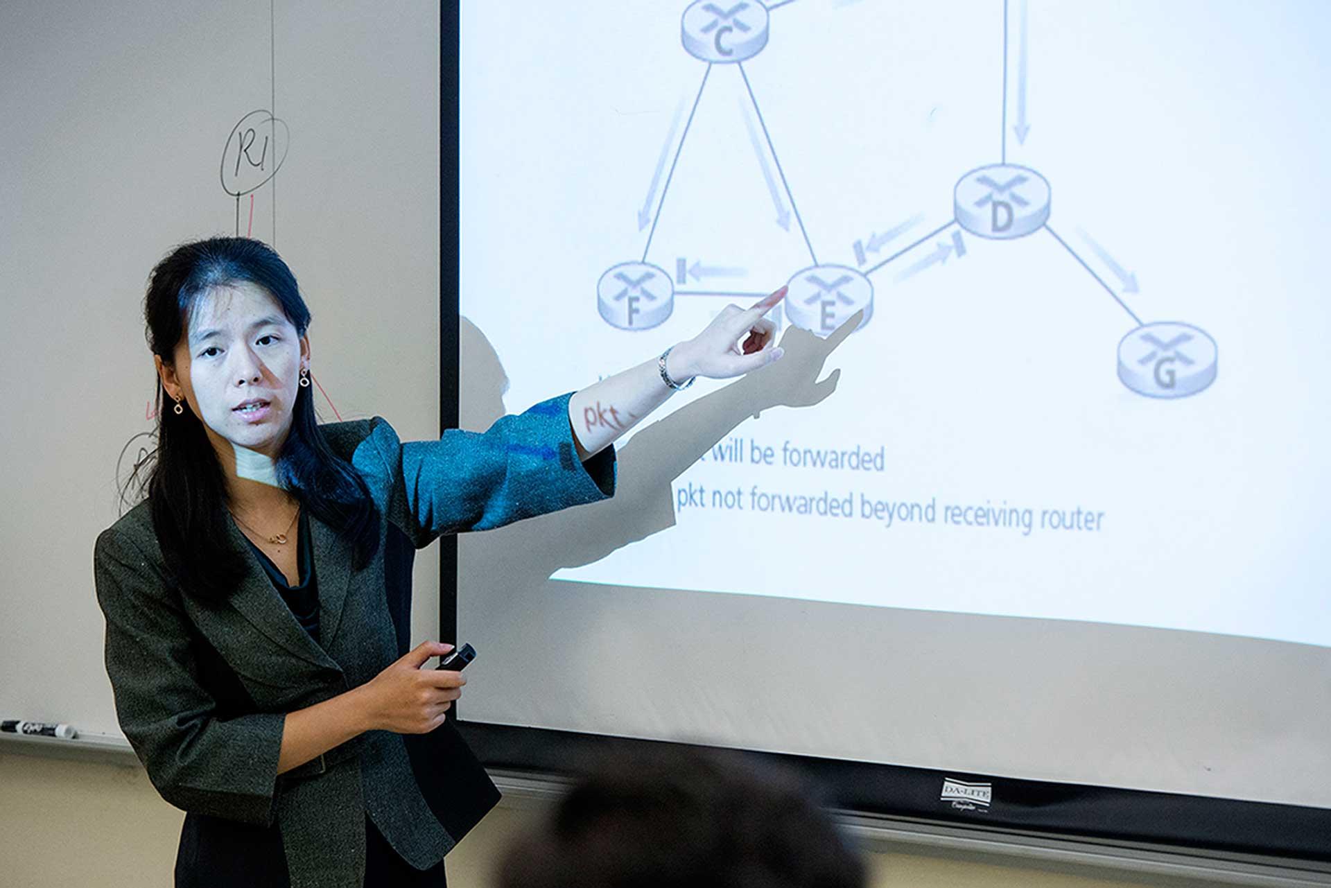 Computer Science professor presenting model on projector screen.